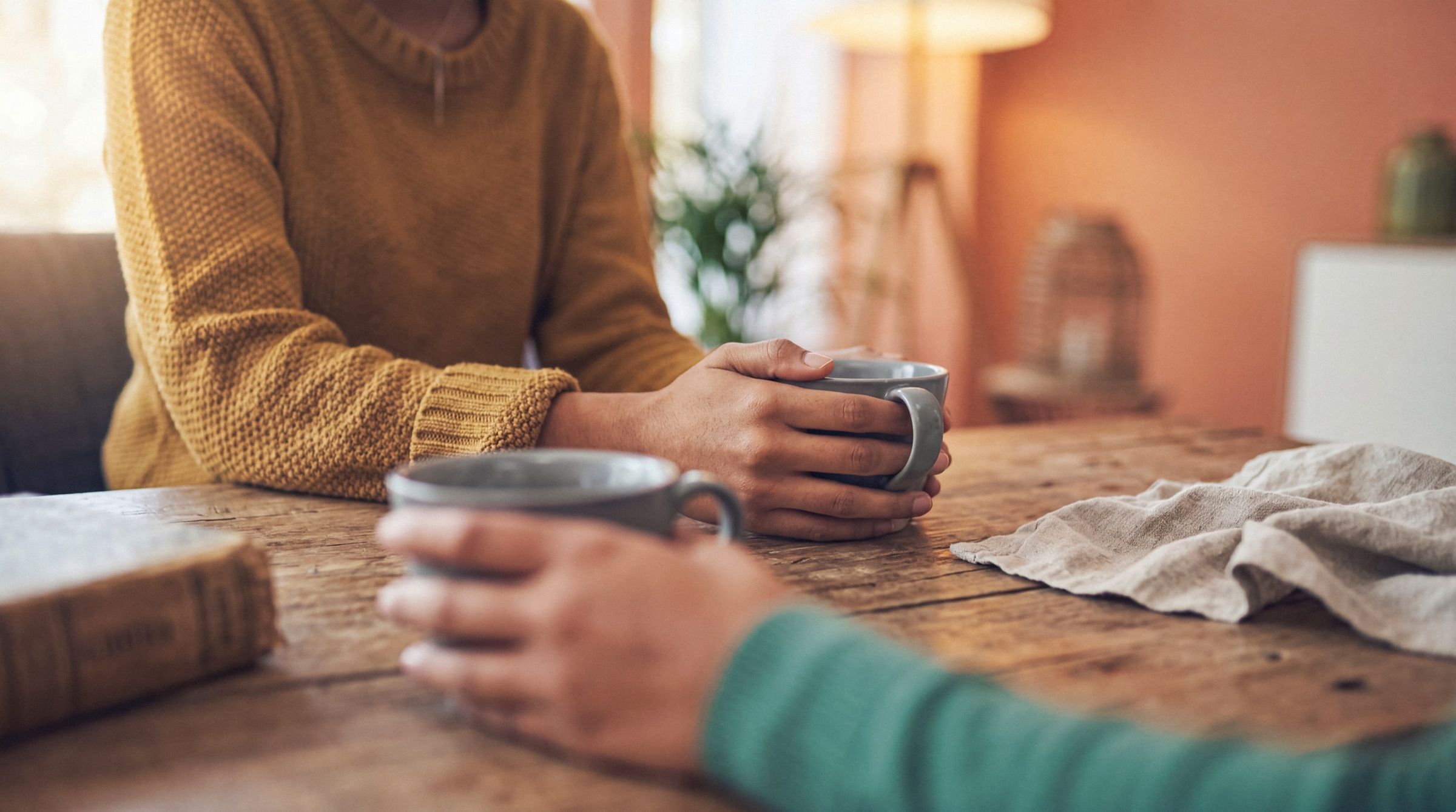 Two people sitting together at a wooden table, each holding a mug of tea